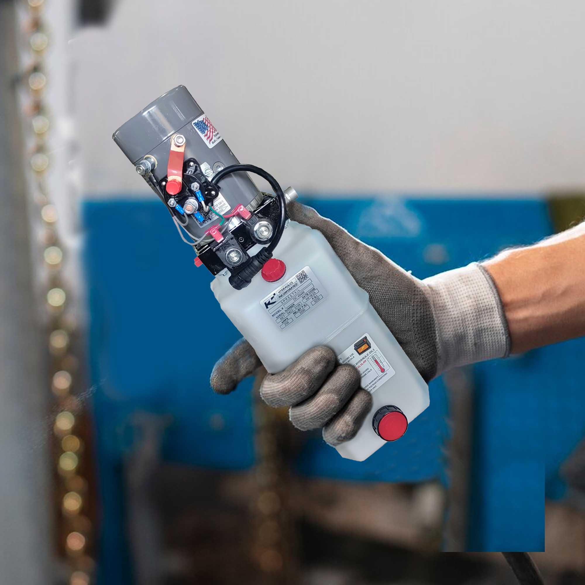Gloved production worker holding a compact KTI hydraulic power unit inside a manufacturing facility.