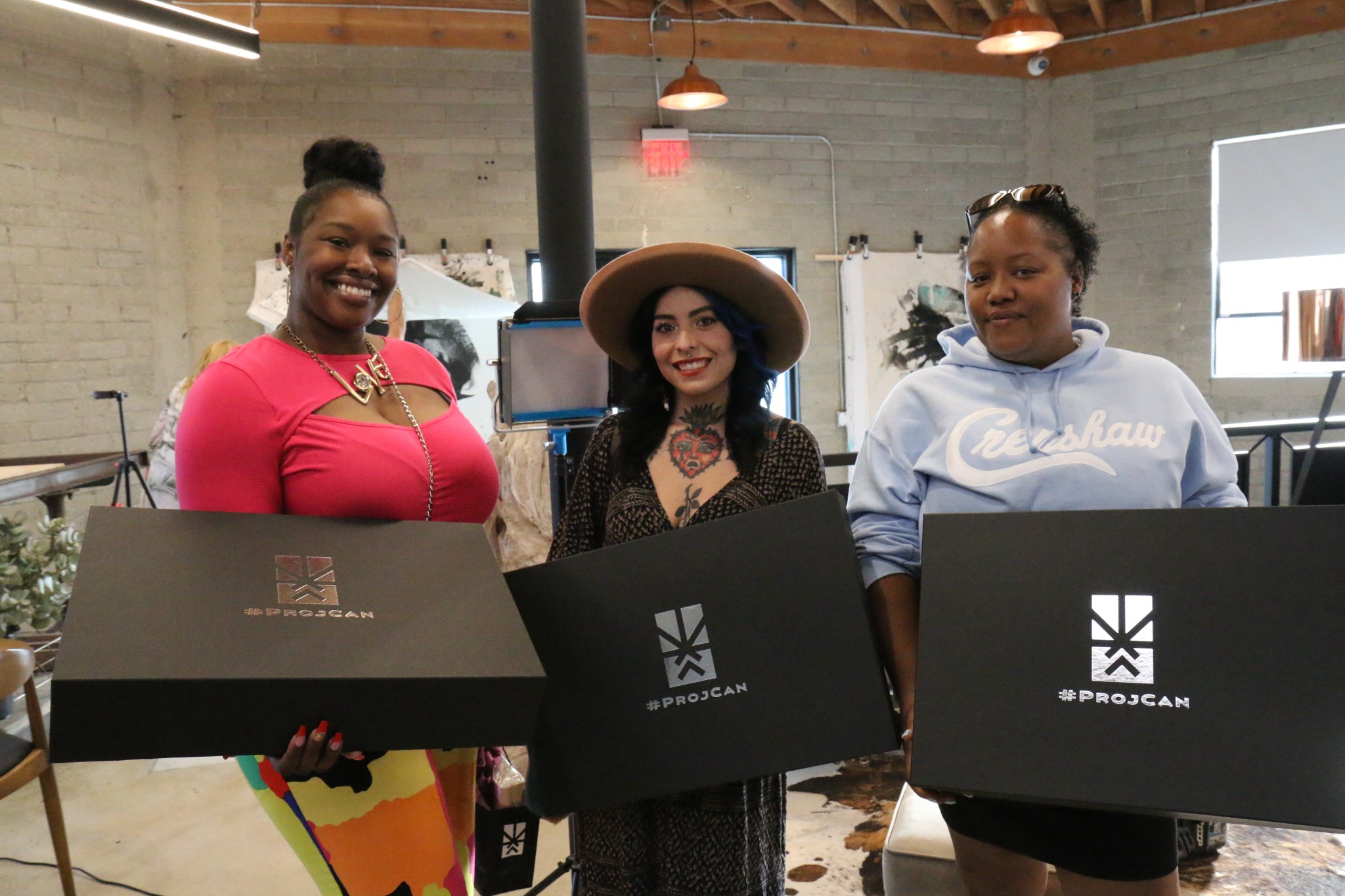 Three I’m ProjCan members holding large black campaign gift boxes during Member Appreciation Day at Project Cannabis headquarters.