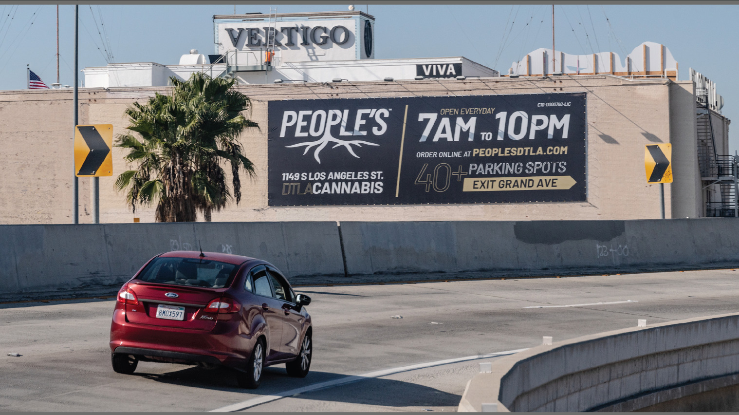 People’s DTLA wallscape installed on a Los Angeles building beside a palm tree and freeway ramp.